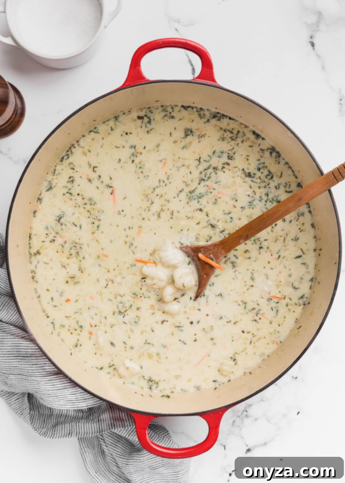 Hearty Chicken Gnocchi Comfort 9 uncooked gnocchi added to soup in a Dutch oven. A wooden spoon sits in the pot.