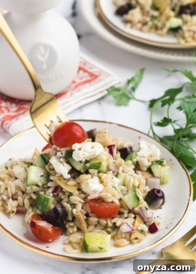 A serving of Orzo Salad with Feta on a white and gold plate, with a gold fork scooping a portion, showcasing fresh ingredients like orzo, feta, and olives.
