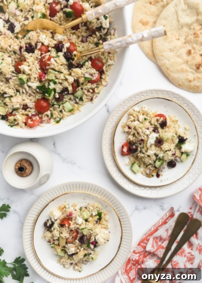Zesty Feta Orzo Salad 8 Overhead view of Orzo Salad with Feta served on individual white plates, alongside a large communal bowl of the salad and warm pita bread rounds.