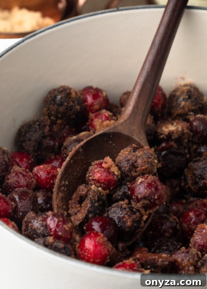 cranberries and cherries tossed with brown sugar and spices on a wood spoon in a white pot 