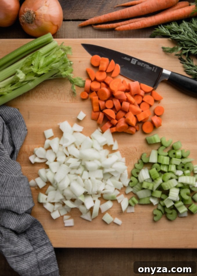 Finely chopped carrots, celery, and onions, forming a classic mirepoix, laid out on a rustic wood cutting board.