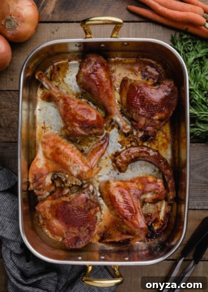 Roasted turkey parts, including wings and drumsticks, glistening golden brown in a copper roasting pan, ready for stock making.