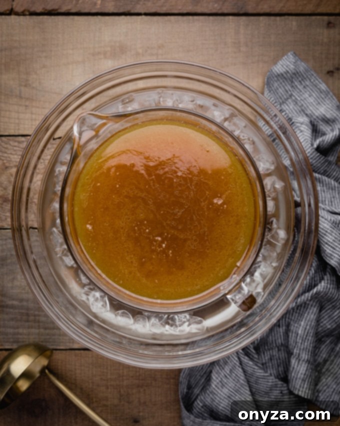 Rich turkey stock in a large glass pitcher, carefully placed within a larger bowl of ice water for rapid cooling.