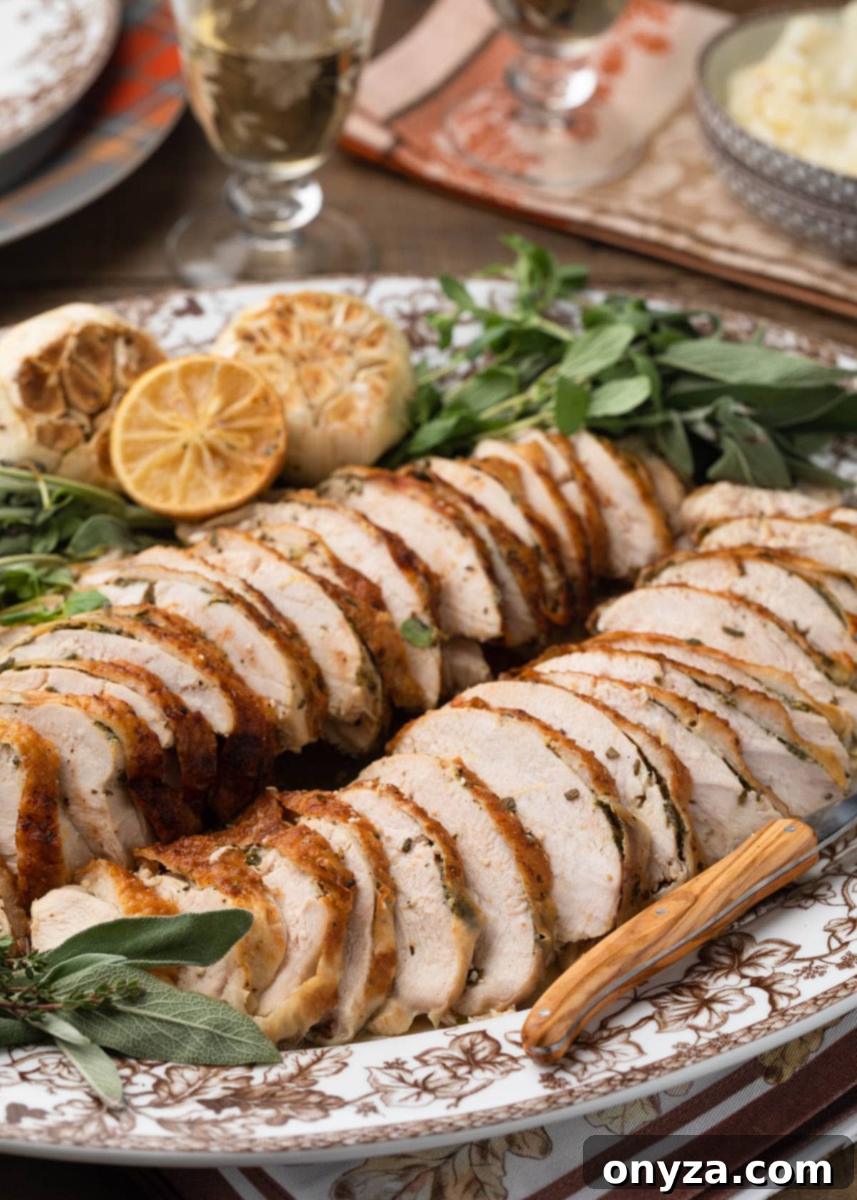 Slices of golden-brown herb roasted turkey breast on a platter, garnished with fresh herbs, roasted lemon, and garlic