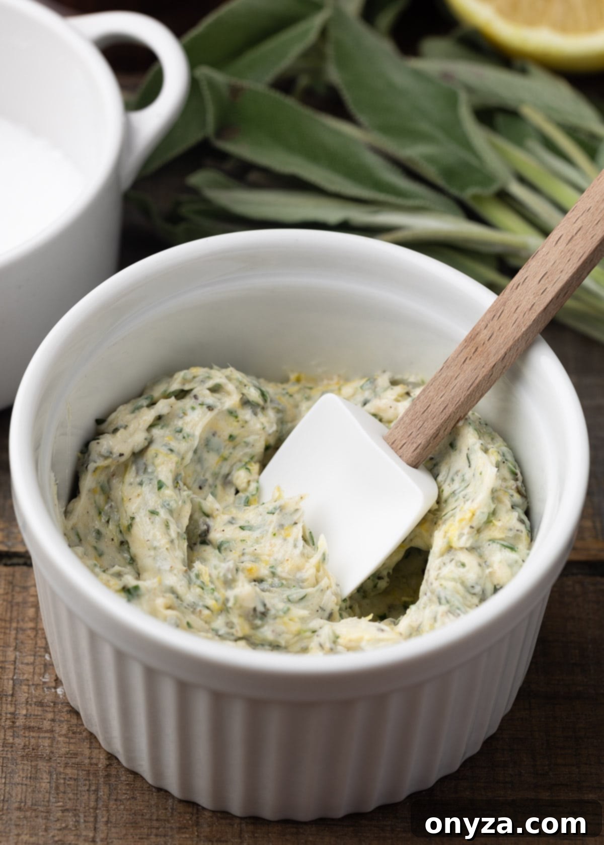 A small white ramekin filled with freshly prepared garlic-herb compound butter, with a miniature spatula for serving