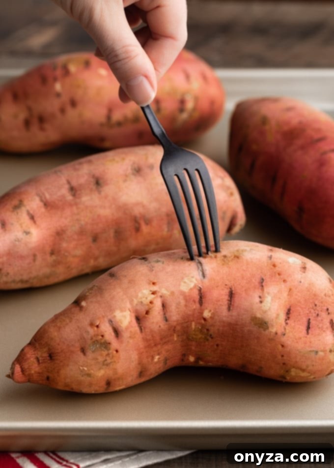 Velvety Brown Butter Sweet Potatoes 4 A fork gently piercing several raw sweet potatoes resting on a baking sheet, ready for roasting.