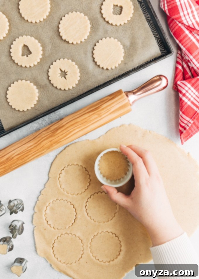 Cutting out rounds of Linzer cookie dough with a fluted cookie cutter on a pastry mat.