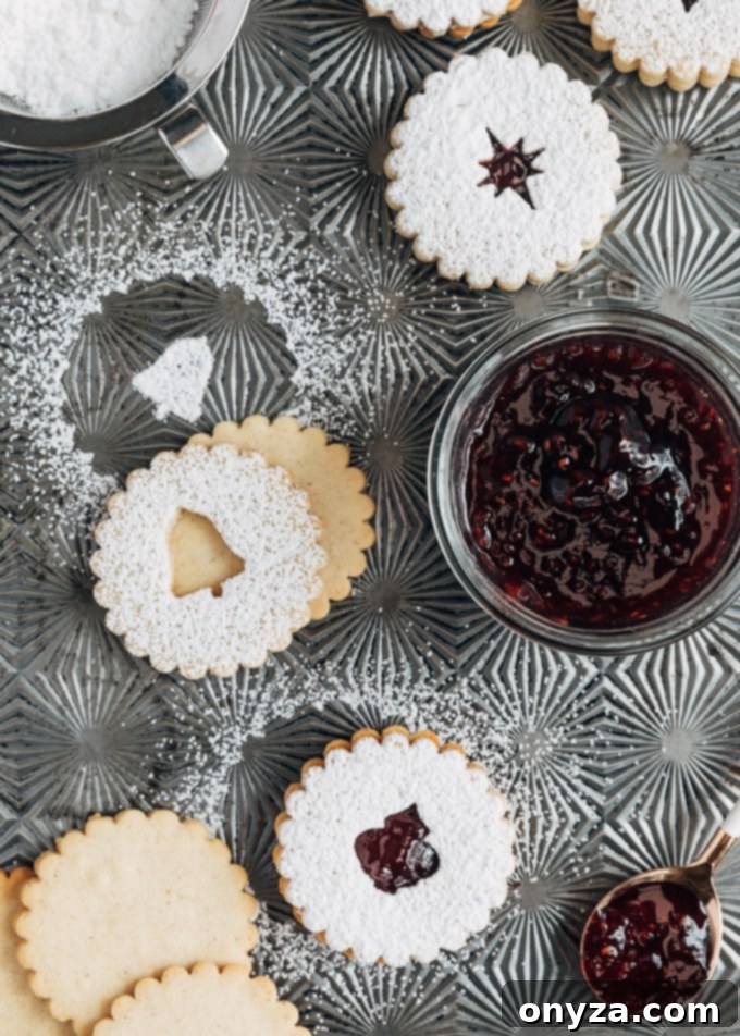 Unassembled and assembled Linzer cookies on a baking sheet, with some dusted with powdered sugar, ready for filling.