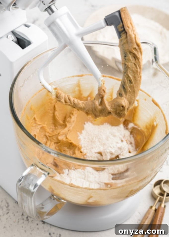 Mixing peanut butter blossom cookie dough in a white KitchenAid stand mixer, showcasing the creamy texture of the ingredients as they combine.