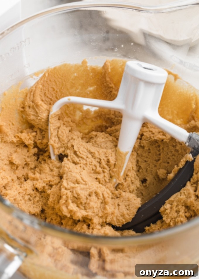 Peanut butter blossom cookie dough in the glass bowl of a stand mixer with the paddle attachment, ready to be chilled and baked.