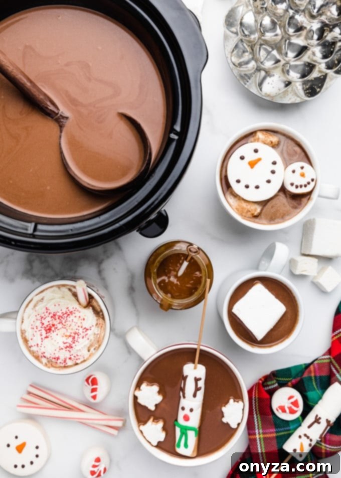 hot chocolate in a crockpot with a ladle, surrounded buy mugs of hot chocolate with snowman and reindeer marshmallows