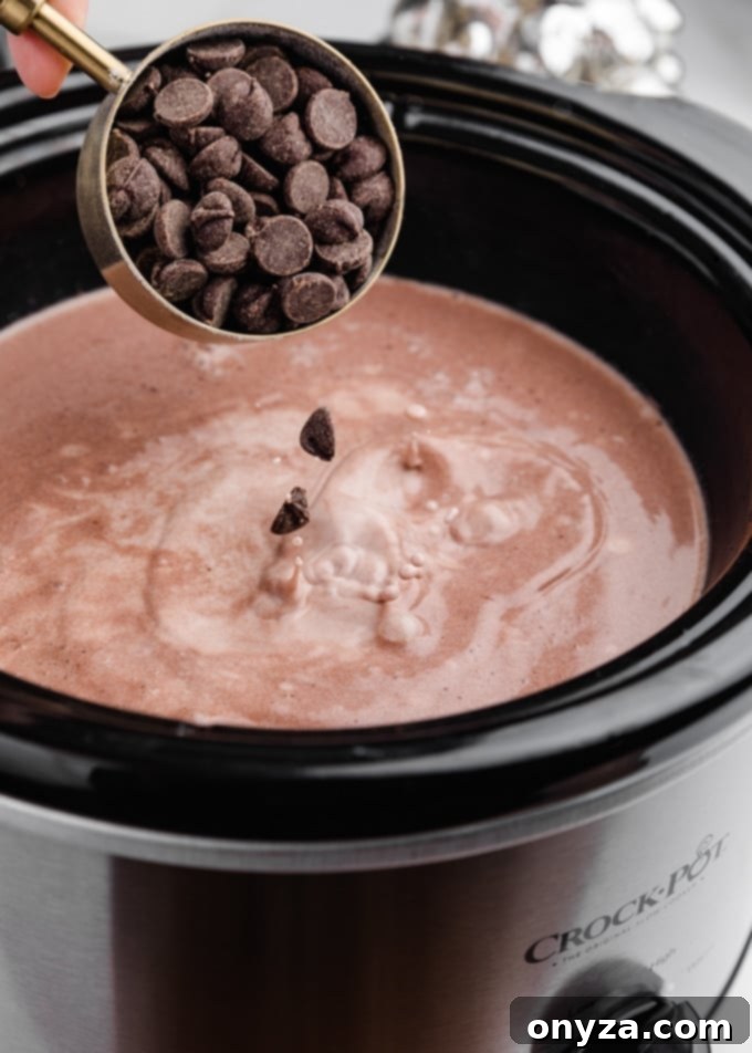 semisweet chocolate chips being poured into a crockpot filled with hot chocolate