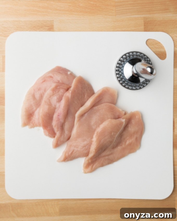 Stovetop and Air Fryer Chicken Milanese 3 chicken cutlets on a white cutting board with a meat mallet