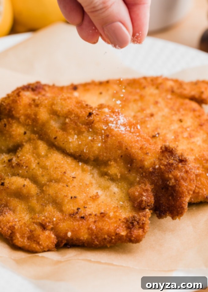 Stovetop and Air Fryer Chicken Milanese 6 sprinkling salt over freshly-fried chicken milanese