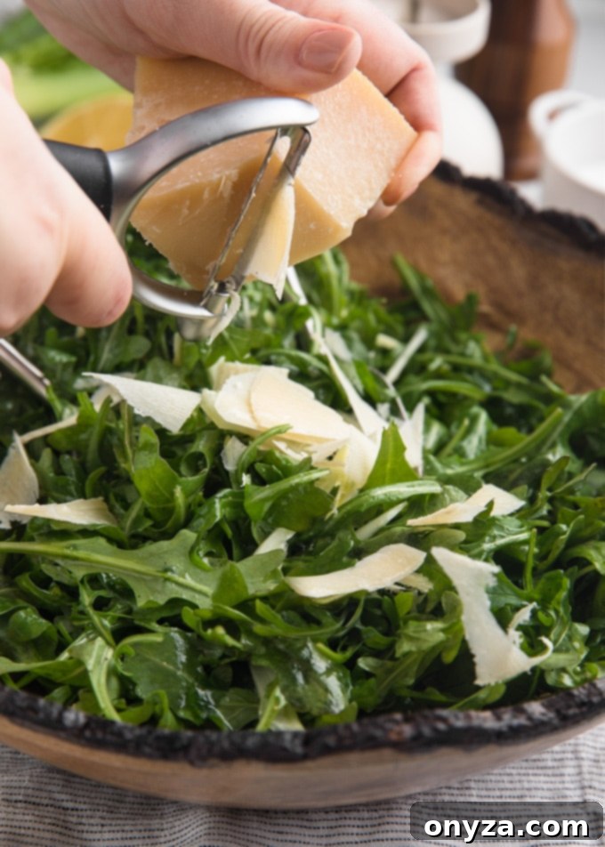 A skilled hand using a vegetable peeler to shave delicate ribbons of Parmigiano Reggiano cheese directly over a vibrant arugula and fennel salad.