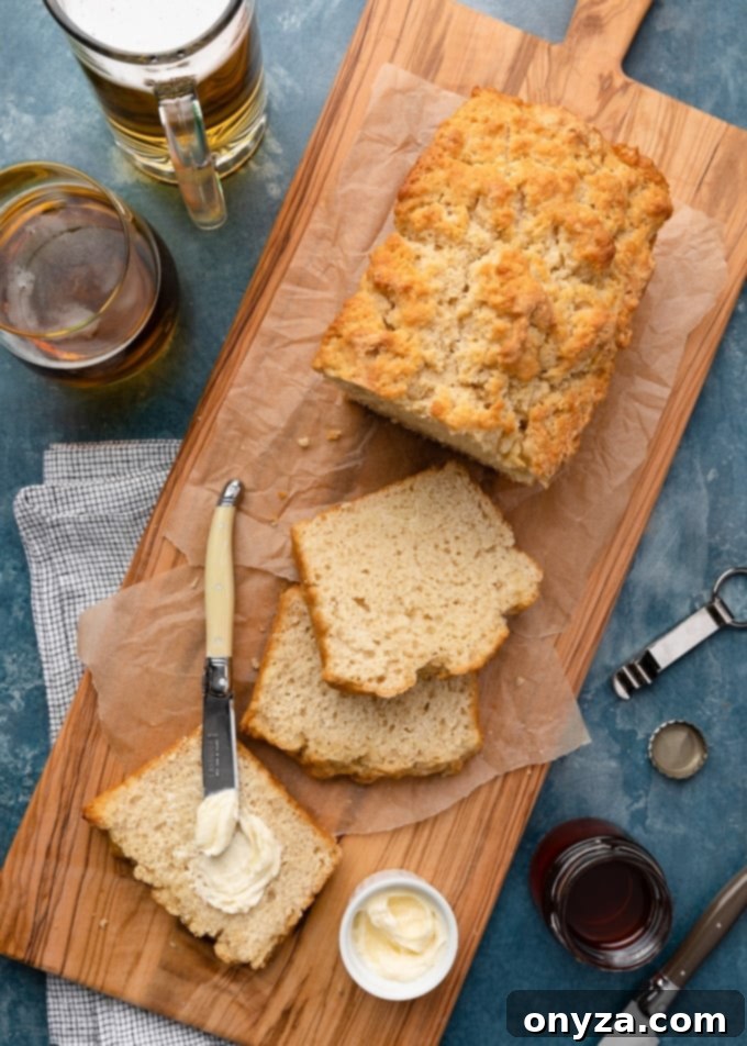 Freshly baked beer bread on a wooden serving board with butter and glasses of lager