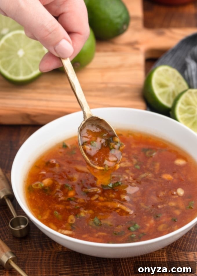 A golden spoonful of vibrant orange dipping sauce being scooped from a pristine white bowl, showcasing its smooth texture and appetizing color.