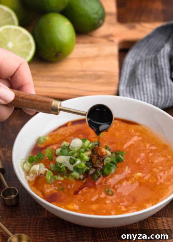 A steady stream of dark soy sauce pours into a white bowl filled with glistening orange marmalade and vibrant green scallions, poised for stirring.
