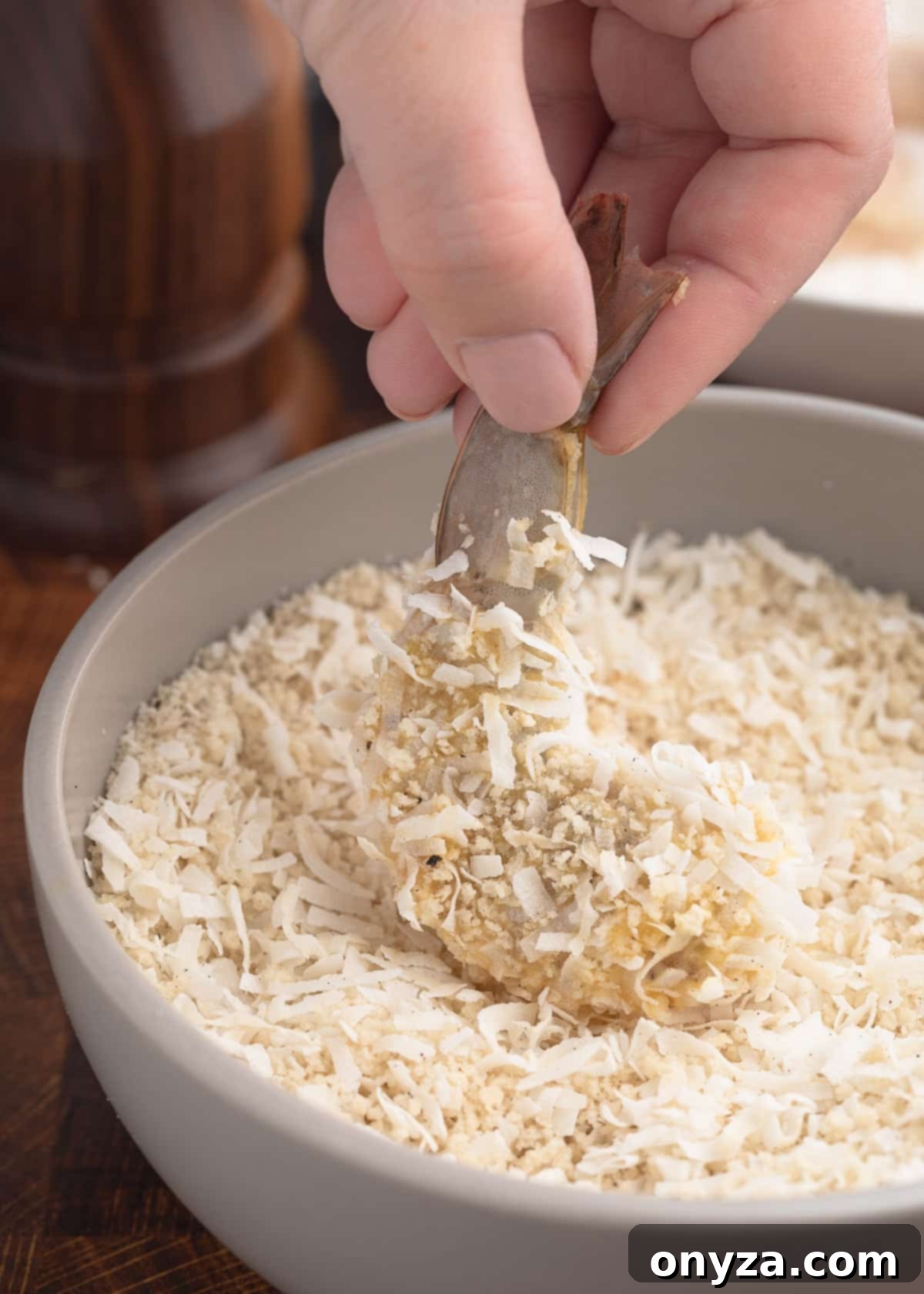 Tropical Crispy Prawns 5 Raw shrimp being carefully coated in a mixture of panko breadcrumbs and shredded coconut in a bowl, ensuring even coverage for a crispy texture.