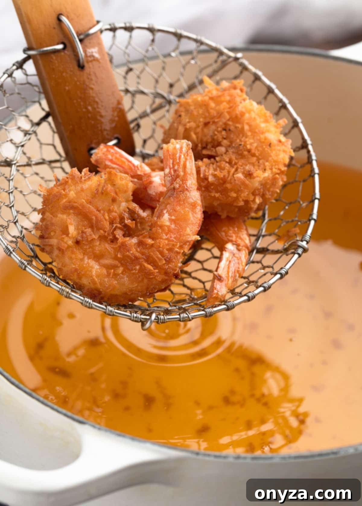 Tropical Crispy Prawns 7 Freshly deep-fried coconut shrimp being lifted from hot oil with a spider strainer, showcasing their golden crispiness.