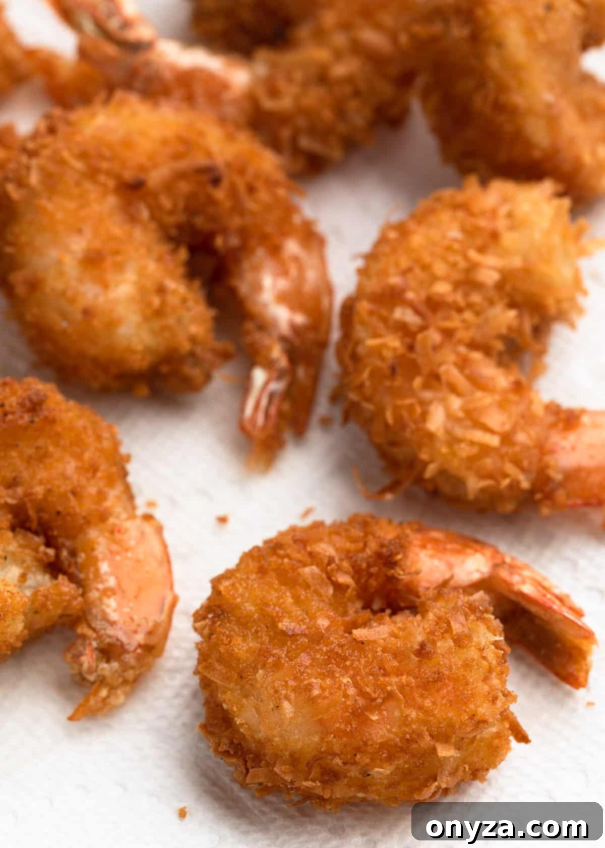Tropical Crispy Prawns 8 Golden-brown deep-fried coconut shrimp draining excess oil on a bed of paper towels, ready for serving.