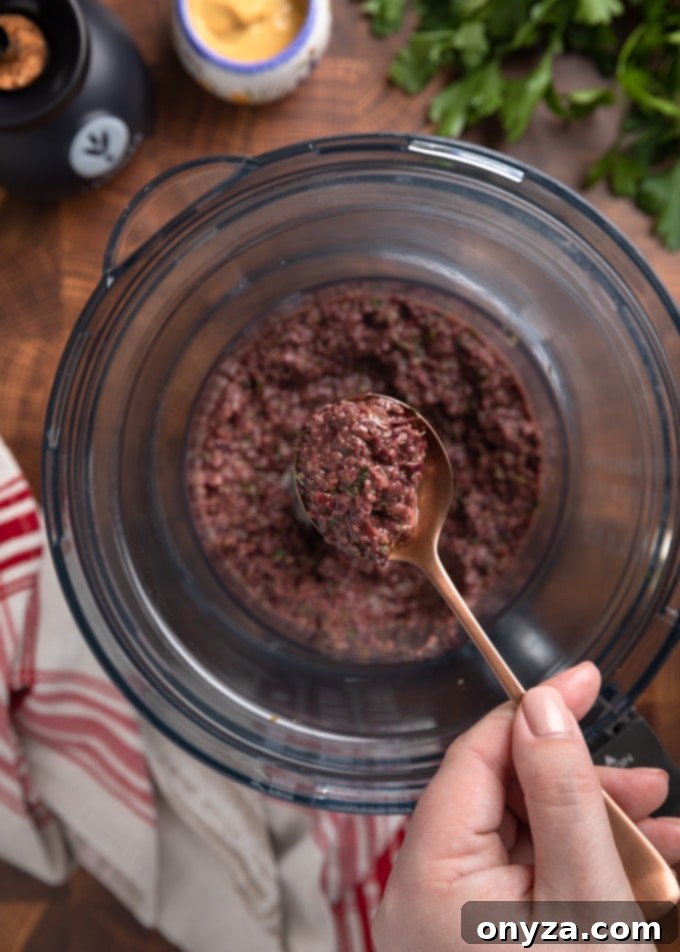 Savory Olive Spread 5 kalamata olive tapenade on a spoon held over the bowl of a food processor