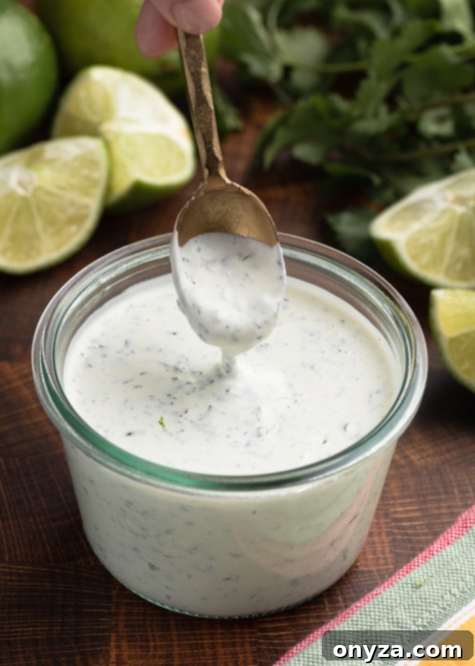 A spoon scooping creamy chipotle lime crema from a glass jar, showing the smooth, orange-hued sauce with flecks of herbs, ready to be served.