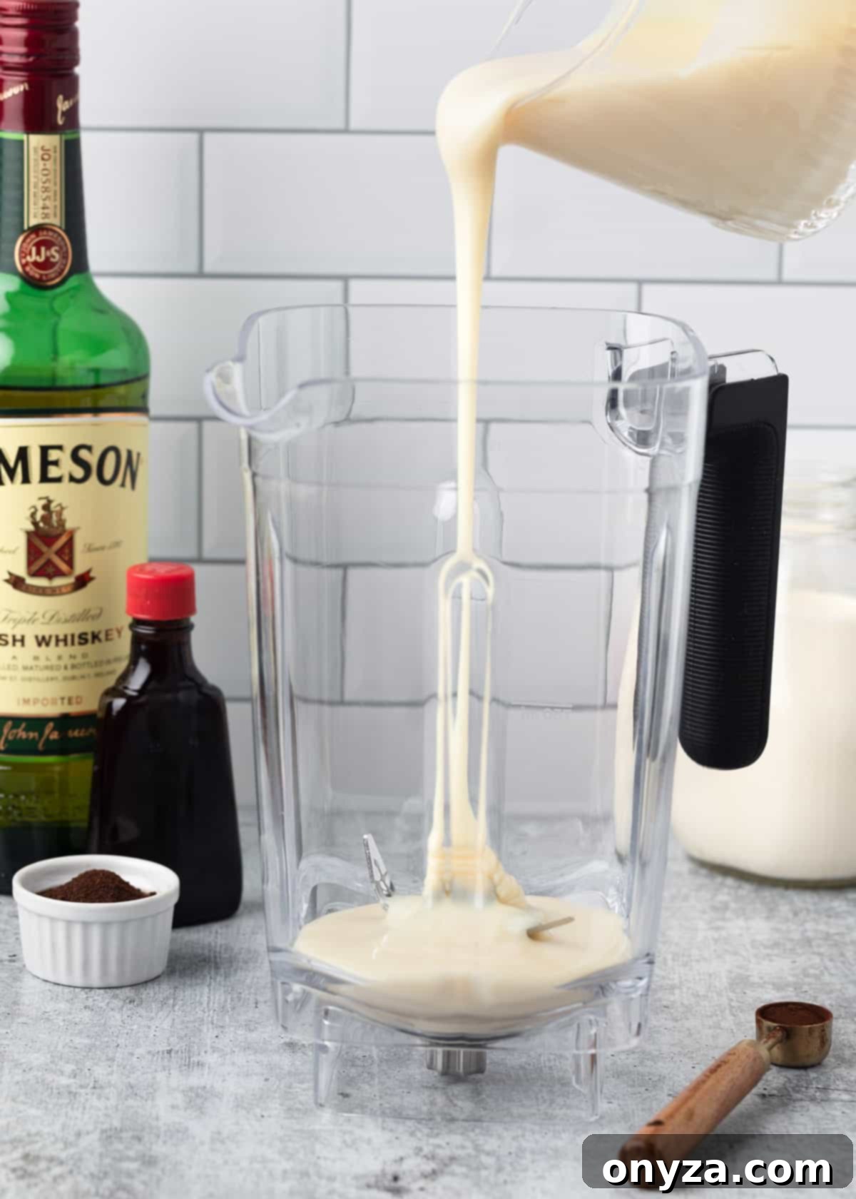 Sweetened condensed milk being poured into a blender canister, forming the base for the homemade Irish Cream.