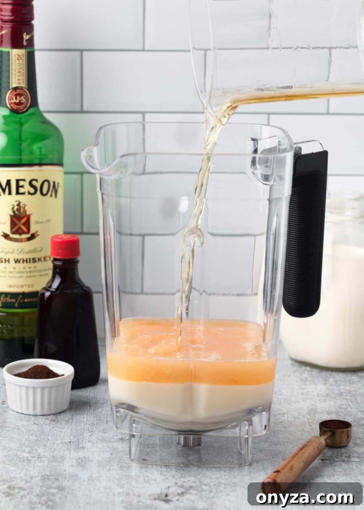 Irish whiskey being carefully poured into a blender canister, mixing with the sweetened condensed milk to begin the Irish Cream blend.
