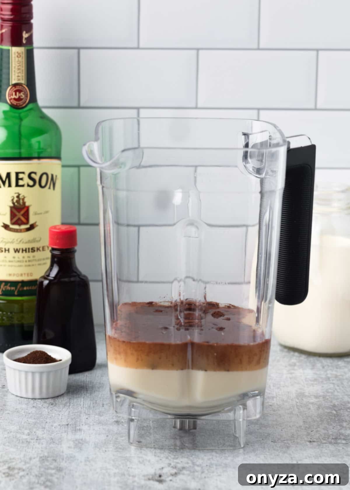 Unblended Irish cream ingredients, including sweetened condensed milk, whiskey, cocoa, coffee, and vanilla, resting in a blender canister, ready for the initial blending stage.