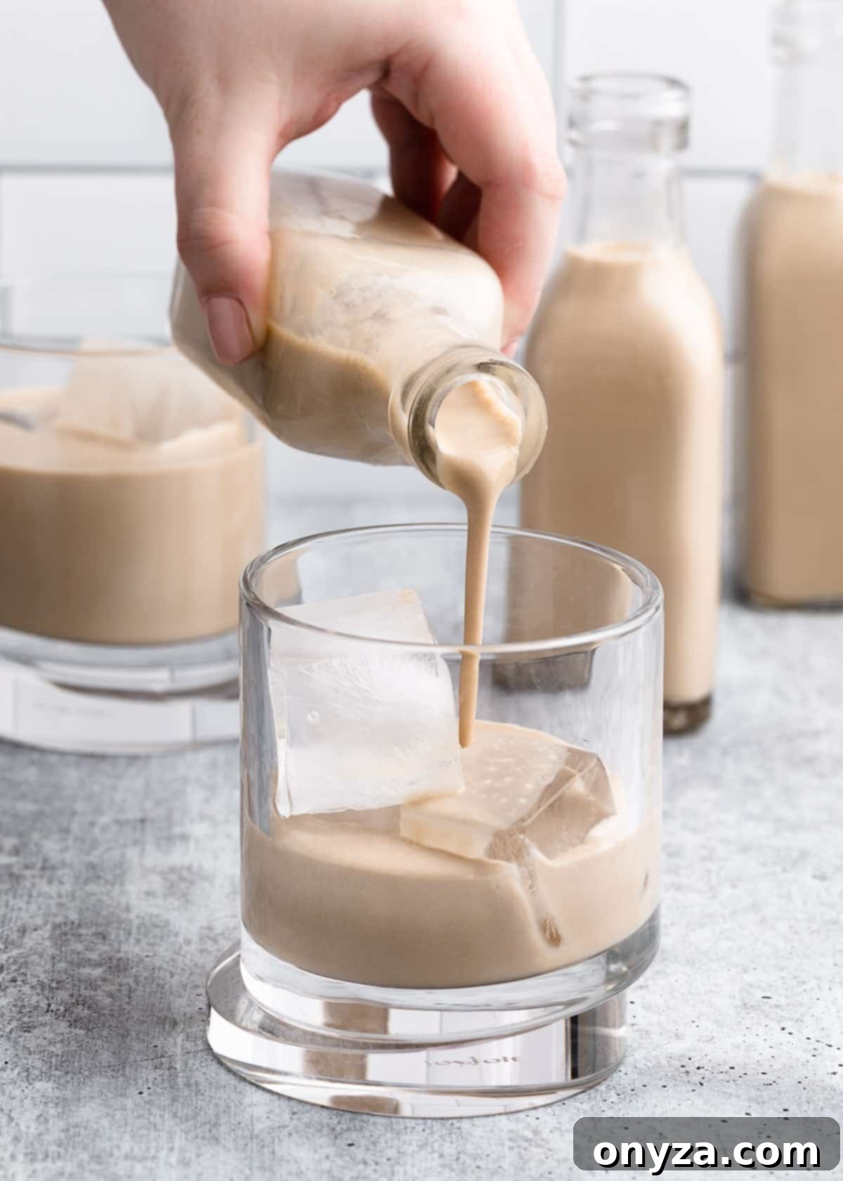 Homemade Irish Cream being poured from a small, elegant glass bottle into a glass filled with ice, ready to be enjoyed as a refreshing and rich beverage.