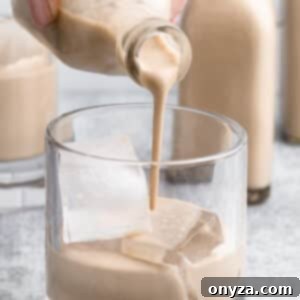 Pouring homemade Irish Cream from a small glass bottle into a glass with ice, ready to serve.