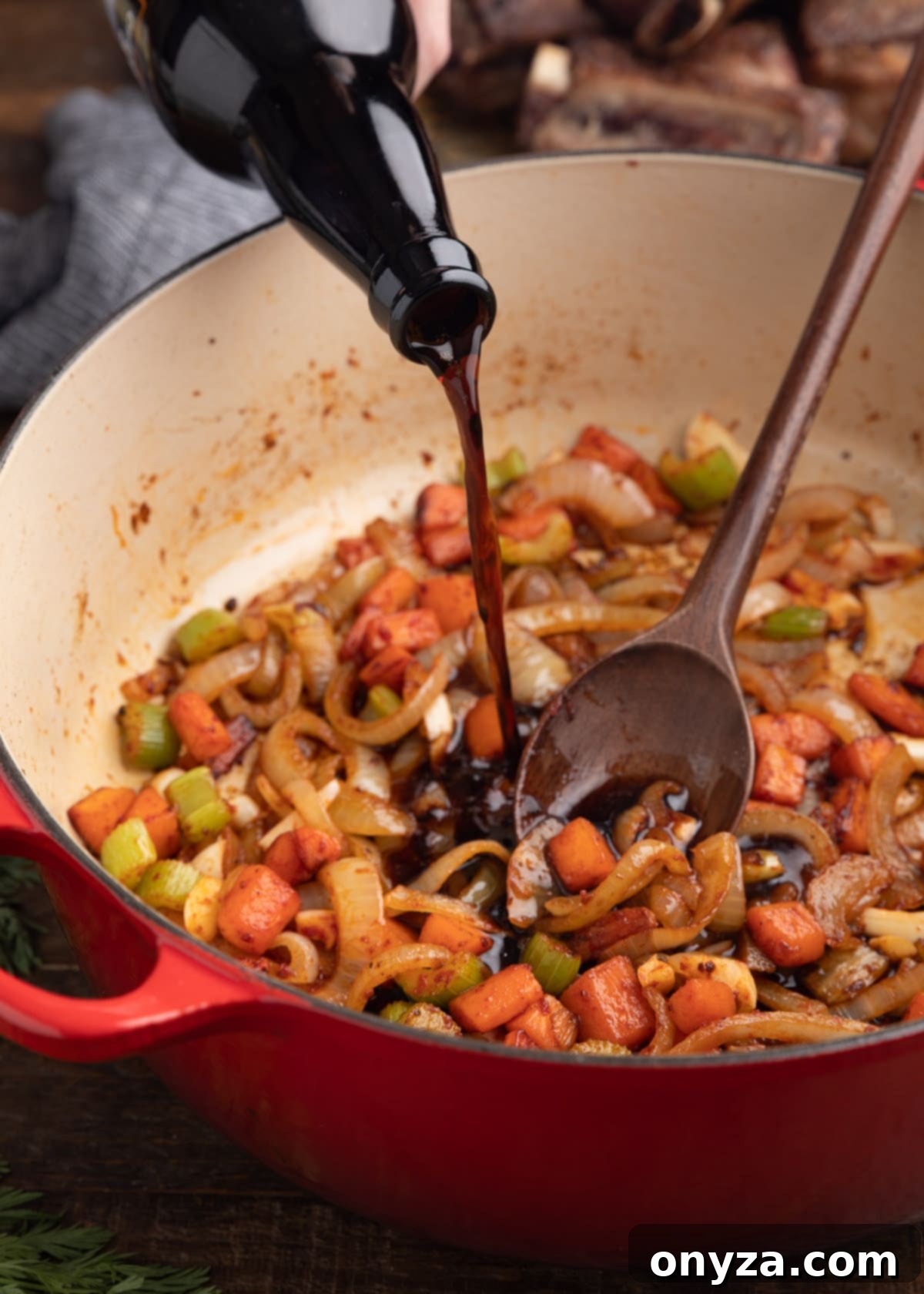 Pouring stout into a Dutch oven with sautéed carrots, onions, and celery, releasing flavorful browned bits