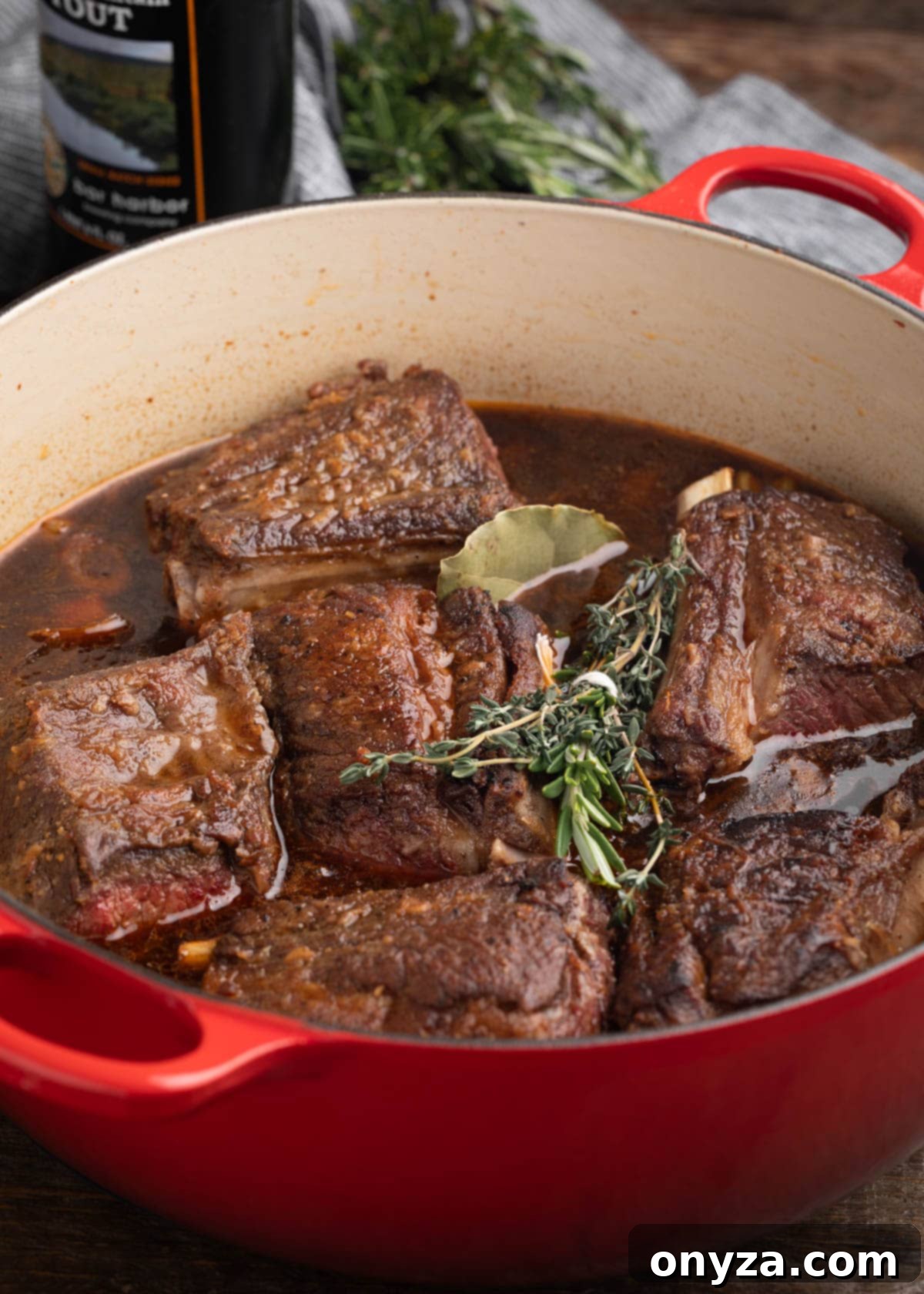 Seared short ribs nestled in an enameled cast iron Dutch oven with herbs and flavorful braising liquid, ready for slow cooking