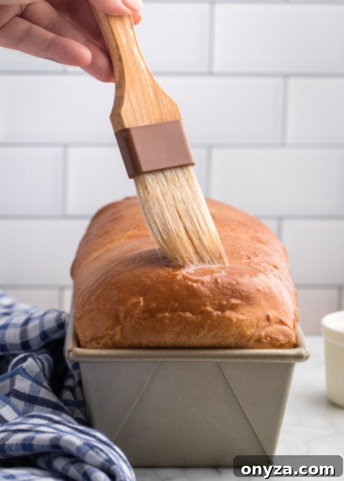 brushing melted butter onto a loaf of homemade white bread