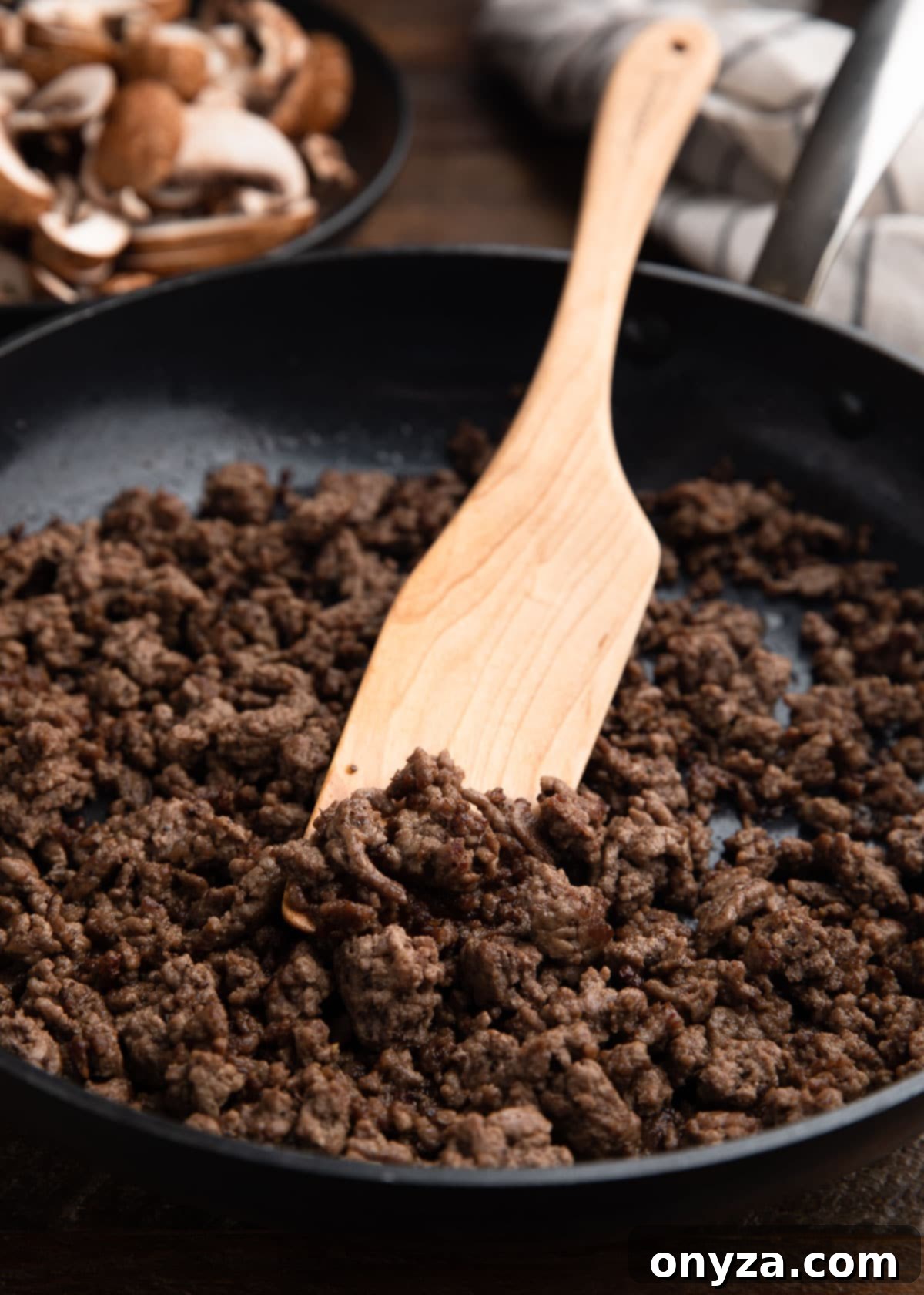 sautéed ground beef in a skillet with a wooden paddle