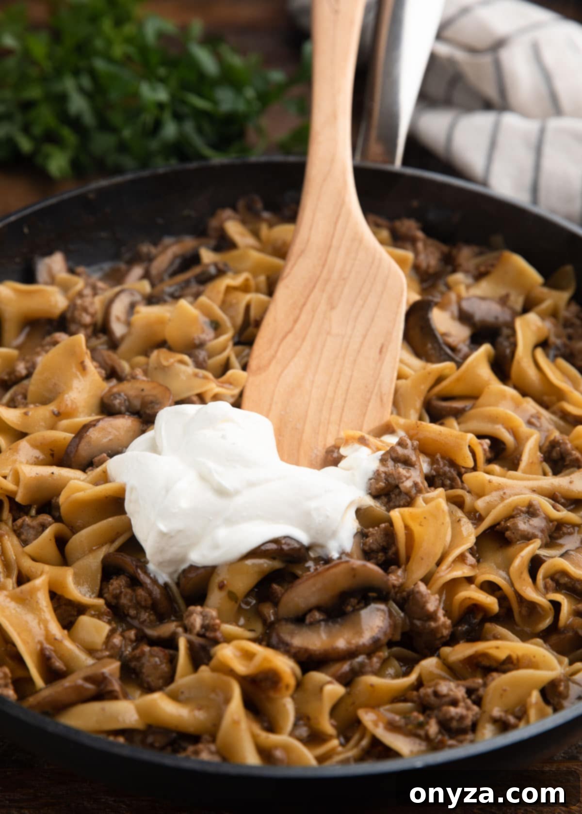stirring sour cream into ground beef stroganoff with a wooden spoon