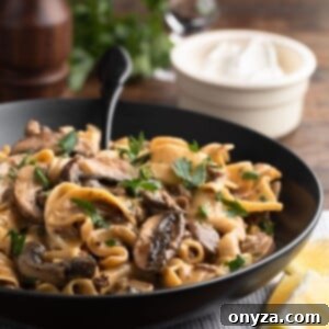 ground beef stroganoff in a black ceramic bowl with a black fork, in front of a bowl of sour cream, a glass of red wine, and a pepper mill