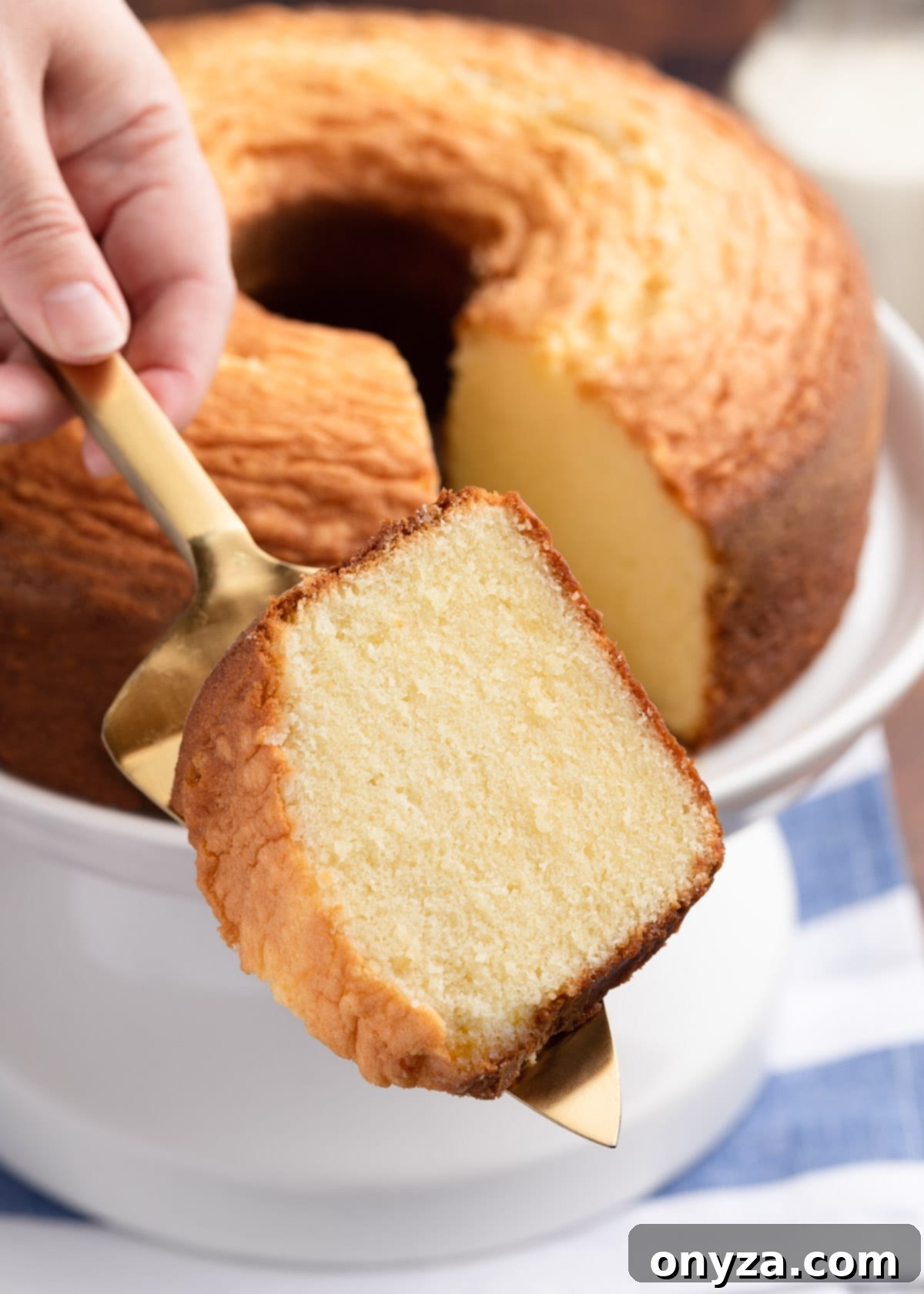 slice of vanilla pound cake on a gold cake server in front of a full pound cake on a white cake stand