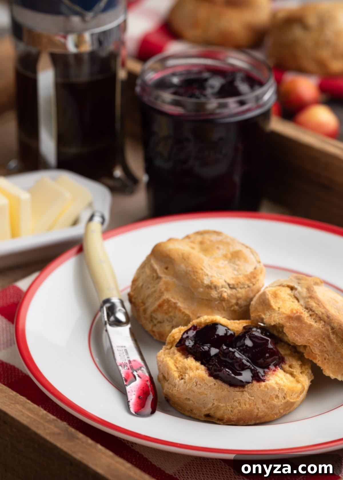 Homemade cherry preserves on a sweet potato biscuit, served on a red-rimmed white plate with a spreading knife.