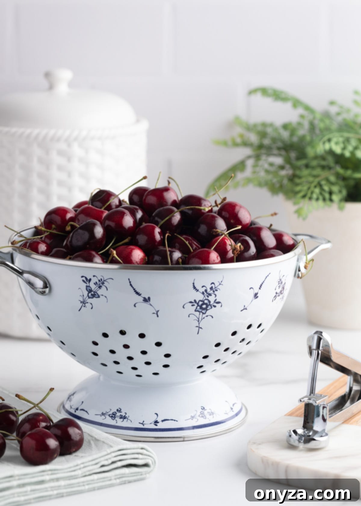 Fresh Bing cherries in a white enameled colander, on a marble countertop against a white subway tile kitchen background.