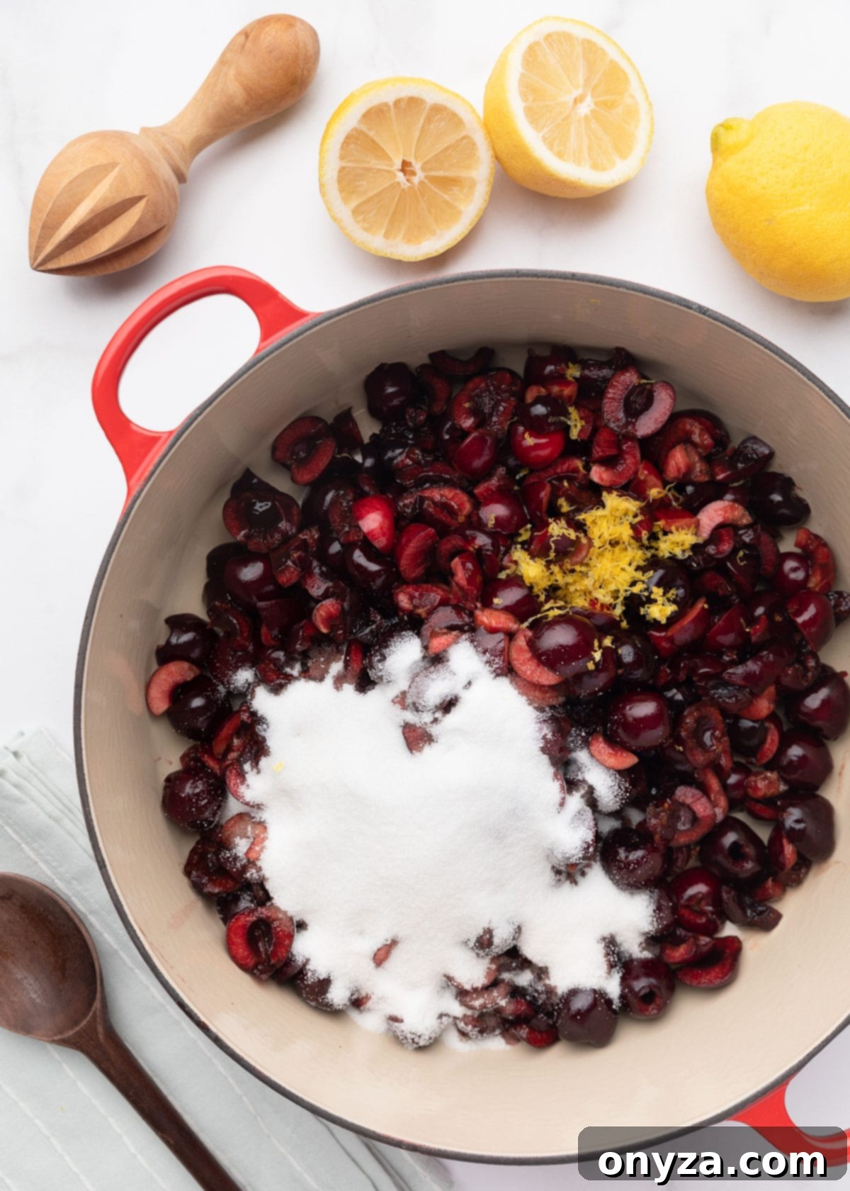 Chopped cherries in an enameled cast iron pot with sugar, lemon juice, and lemon zest.