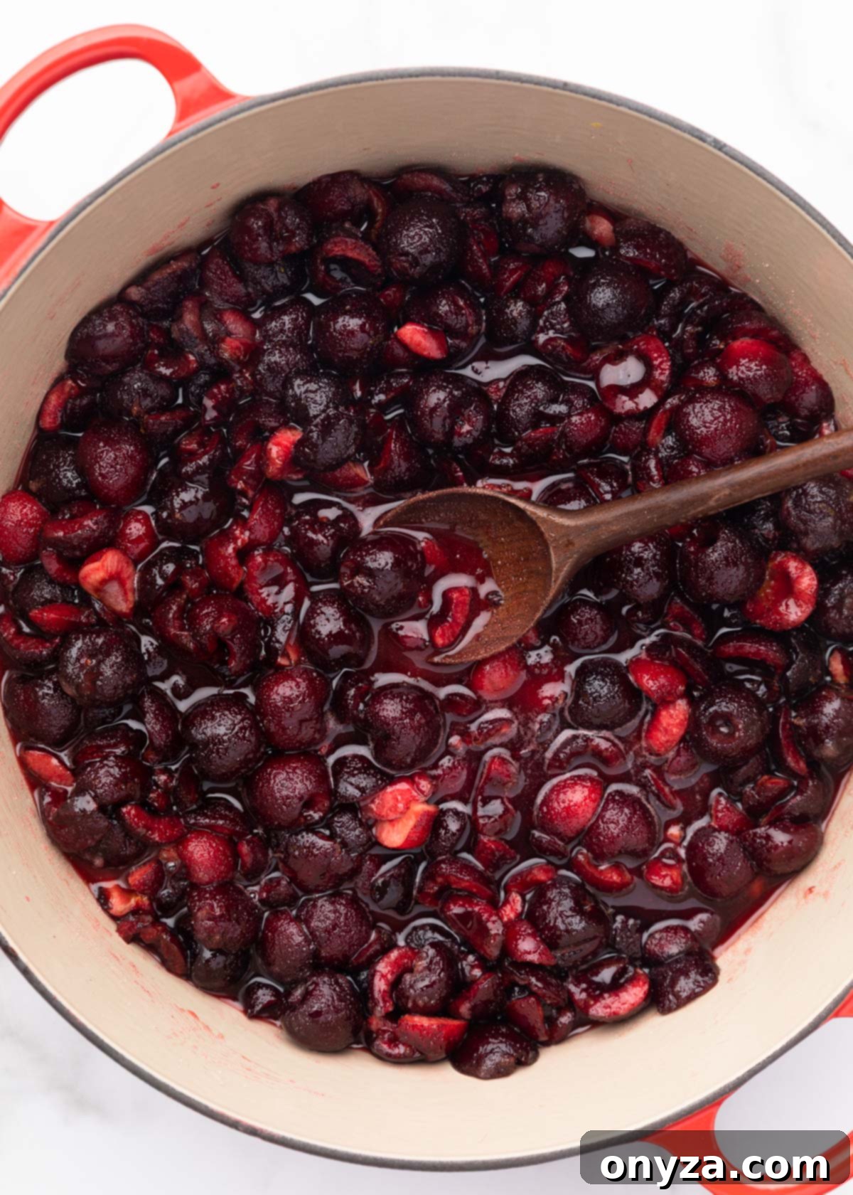 Macerated Bing cherries in an enameled cast iron pot with a wooden spoon.