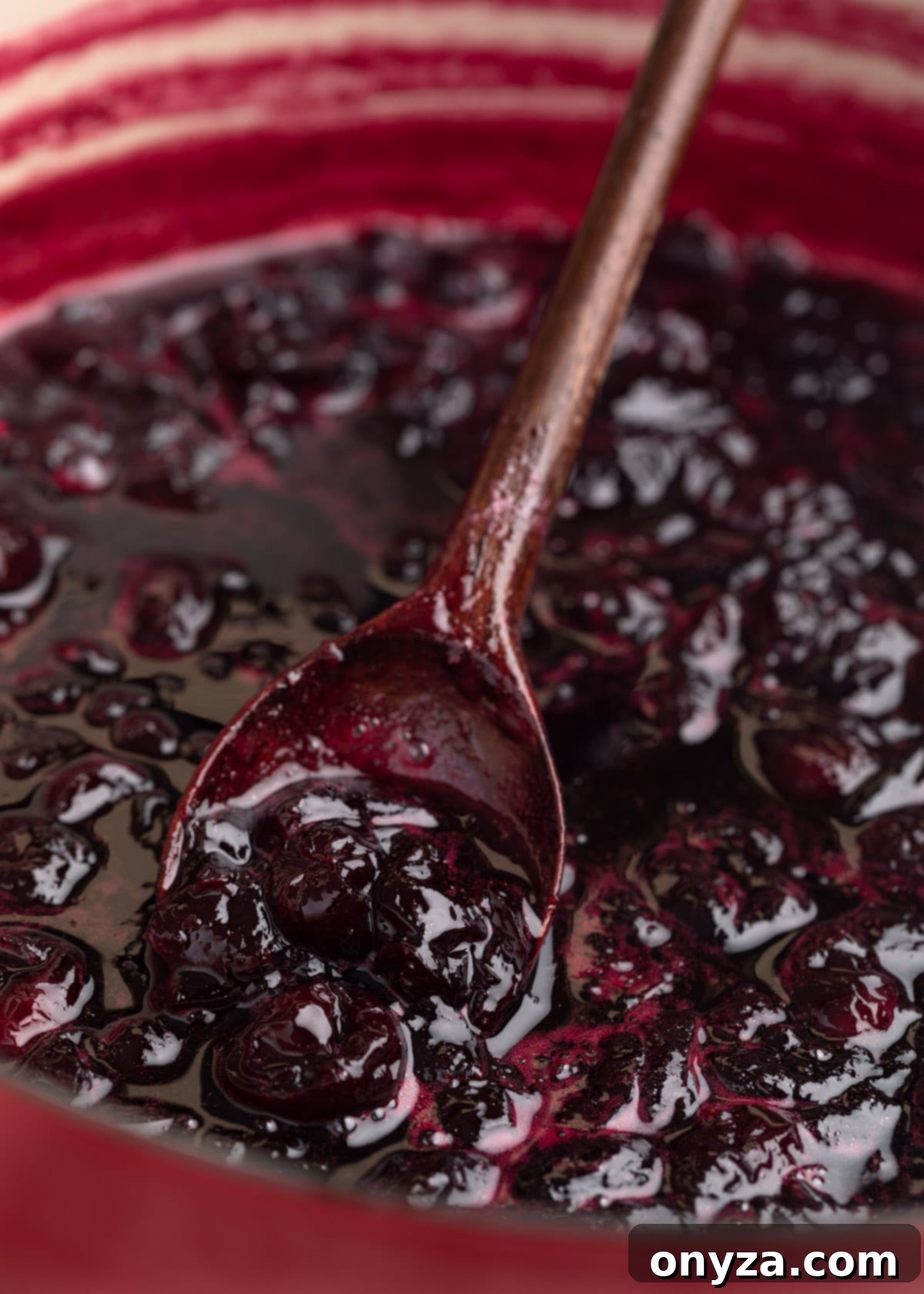 Cooked cherry preserves in a pot on a wooden spoon.