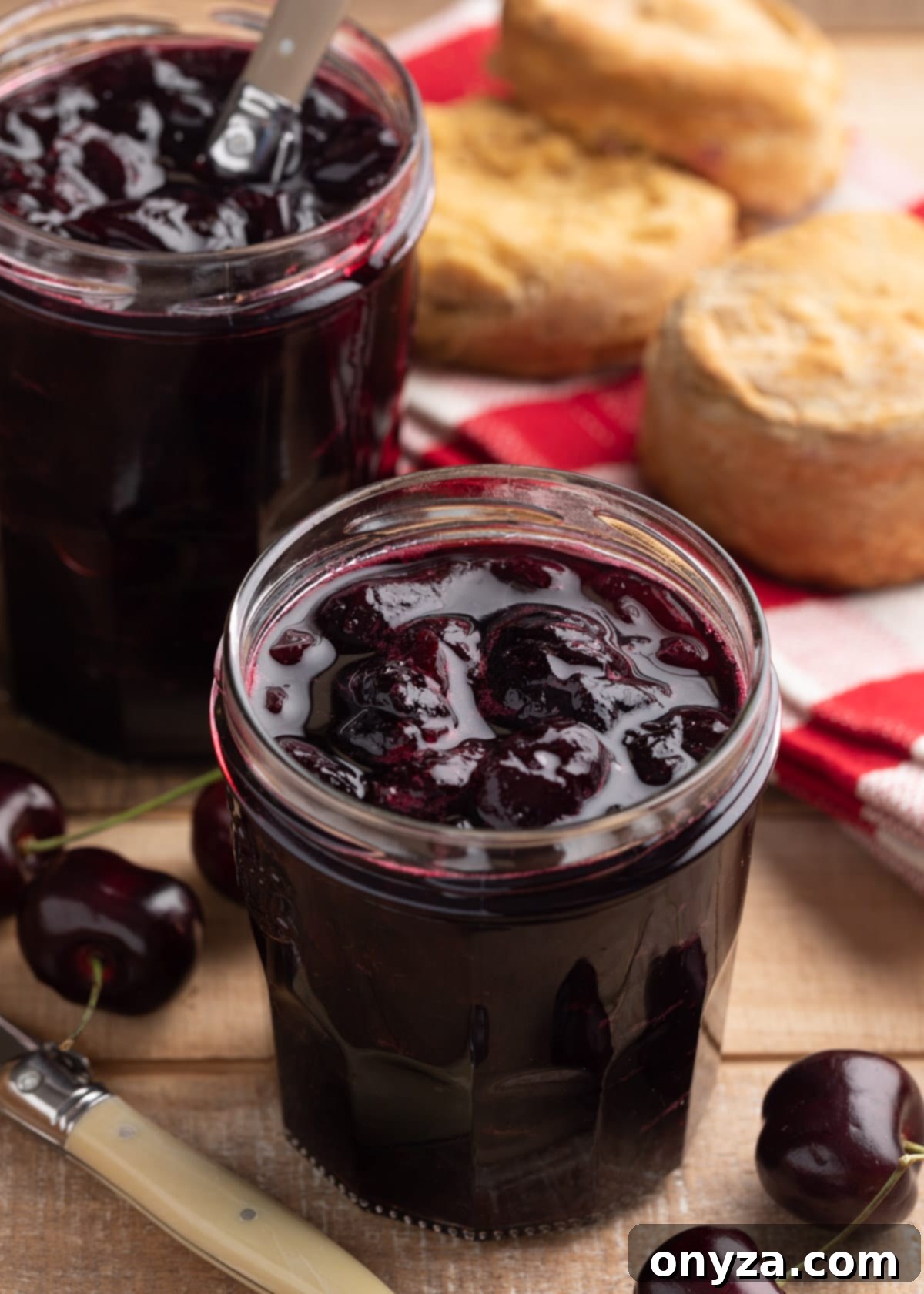 No-pectin cherry preserves in glass jam jars on a wood board.