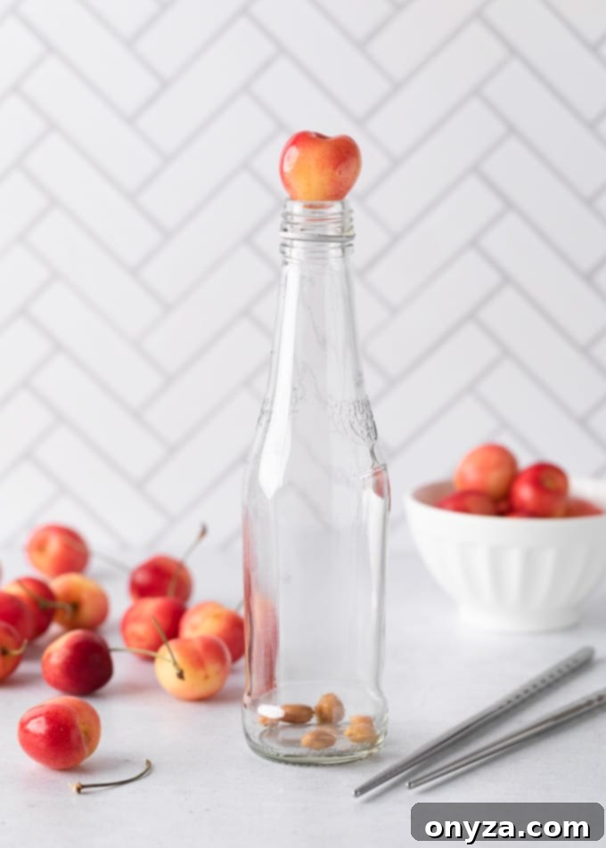 A rainier cherry sitting on top of a glass soda bottle holding cherry pits in the bottom, surrounded by more cherries and a pair of metal chopsticks.