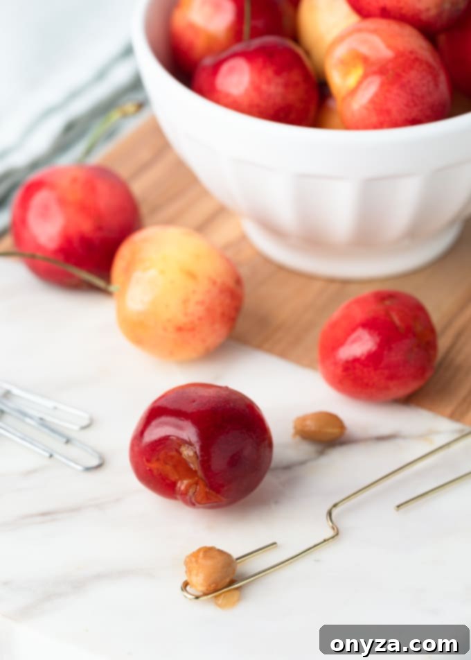 cherry pit sitting on a bent gold paperclip next to rainier cherries on a white marble cutting board