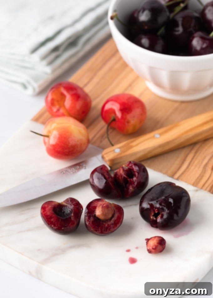 Bing cherries on a marble cutting board with a paring knife showing three cutting techniques for cherry pitting.