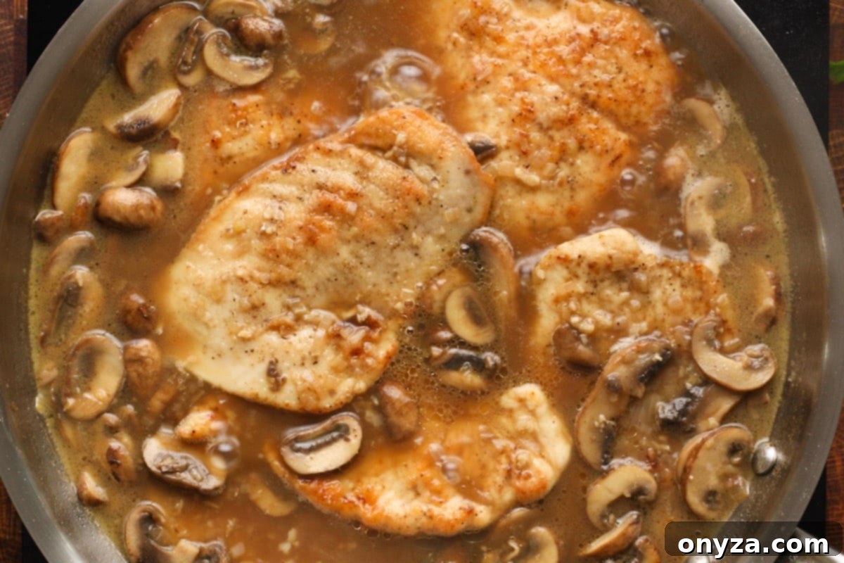 Chicken cutlets and mushrooms simmering gently in a rich Marsala wine sauce in a pan, absorbing all the wonderful flavors.
