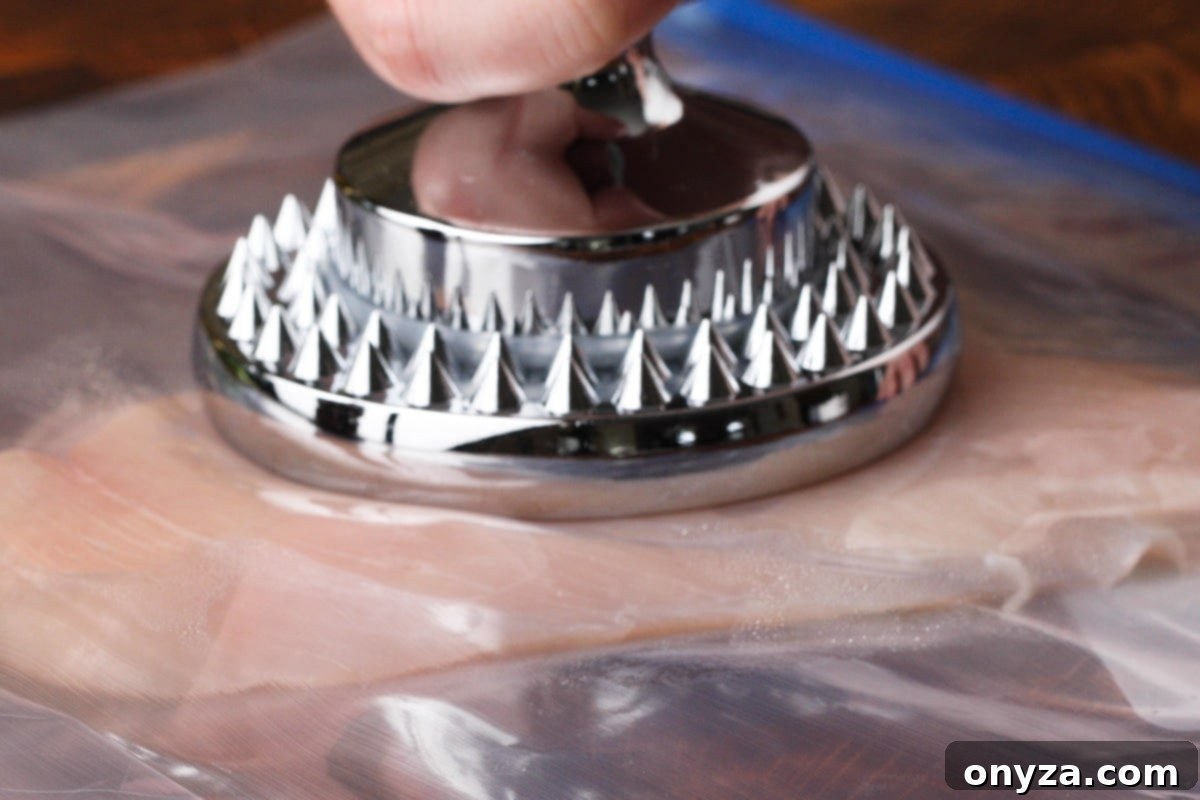 A chicken cutlet being pounded to an even thickness using a stainless steel meat pounder, enclosed in a zip-top bag.